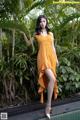 A woman in an orange dress standing next to a pool.