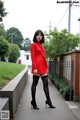 A woman in a red coat and black stockings posing for a picture.