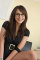 A woman wearing glasses sitting on a chair in an office.