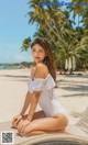 A woman in a white swimsuit sitting on a beach.