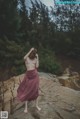 A naked woman standing on a rock in the woods.