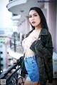 A woman in a camo jacket and denim shorts posing on a balcony.